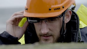 A worker wearing a helmet and protective clothing. He is looking through data goggles.